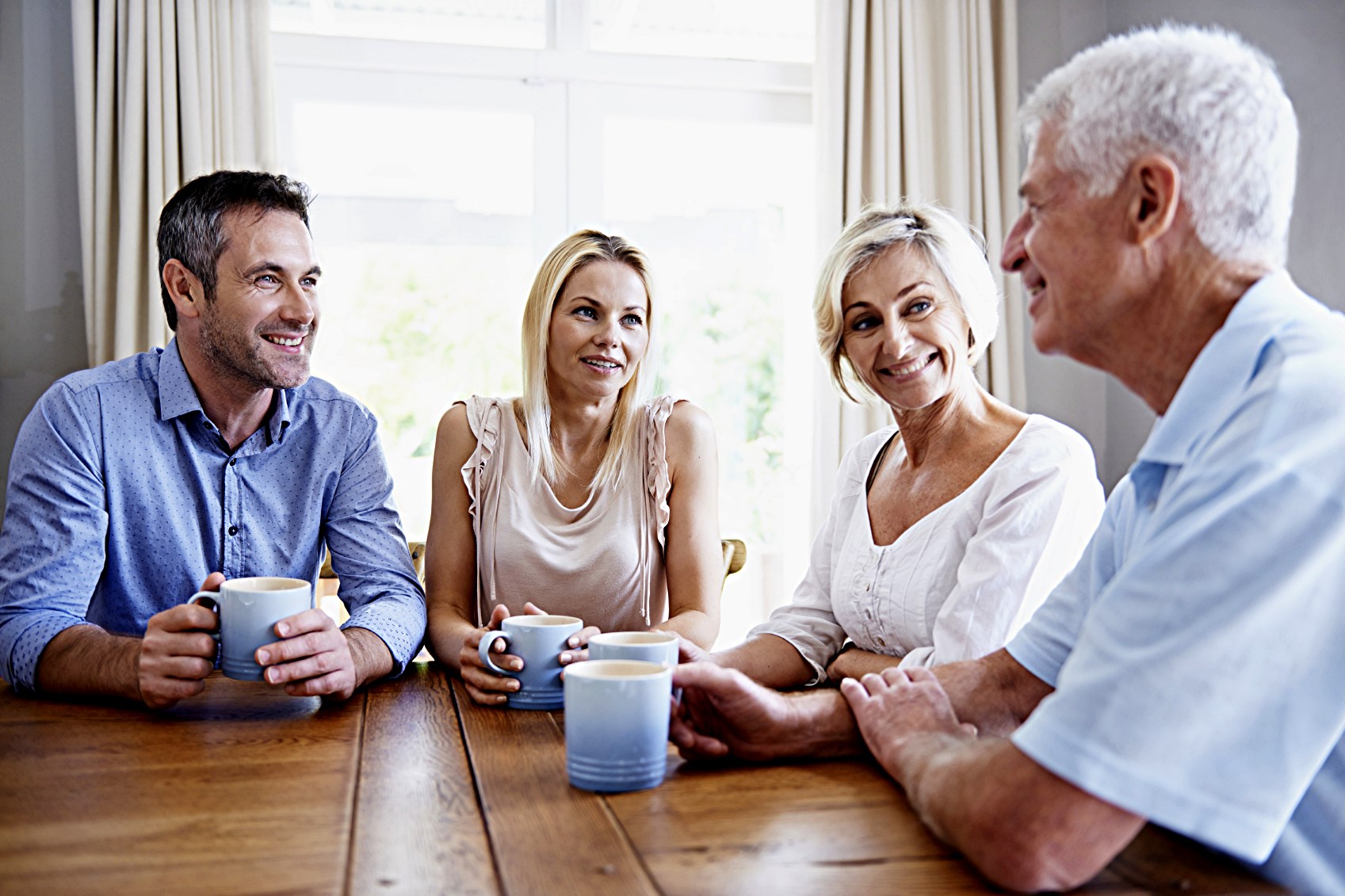 An older couple and a younger couple drinking coffee at the table, smiling because the older man has learned to tell better stories